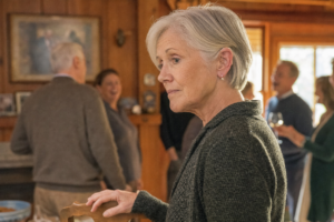 Older woman wearing a hearing aid standing slightly apart from a family gathering in warm late-afternoon light